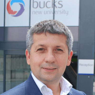 Head and shoulders picture of a smiling Florin Ionas stood outside of BNUs High Wycombe reception with the BNU logo on show